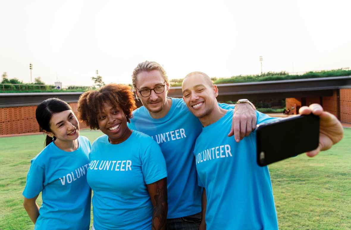 four person taking selfie while wearing blue volunteer t shirt